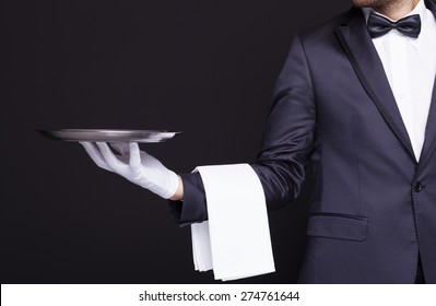 Waiter holding an empty silver tray against dark background