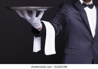 Waiter holding an empty silver tray against dark background