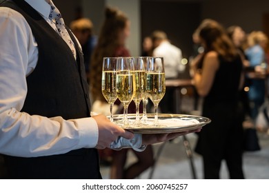 A waiter is holding a plate with sparkling wine to welcome people at an event. Glasses with champagne to toast. Drinks at a luxury party in a hotel. - Shutterstock ID 2060745257