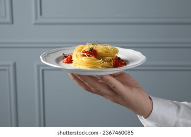 Waiter holding plate of tasty capellini with tomatoes and cheese near grey wall, closeup. Exquisite presentation of pasta dish - Powered by Shutterstock