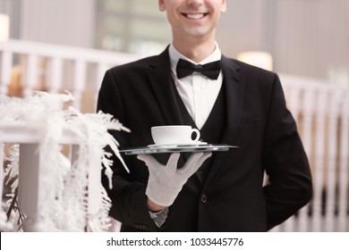 Waiter holding tray with cup of coffee indoors