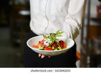 Waiter holds a plate with tasty dish, traditional Italian Greek salad. Waiter wearing white uniform in a restaurant. - Powered by Shutterstock