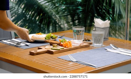 Waiter at a luxury outdoor tropical restaurant serves fresh, delicious food. Close-up of hands placing plates on an elegant table. Fine dining service. - Powered by Shutterstock