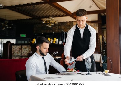 The waiter makes an exquisite serving of seafood salad, tuna and black caviar in a beautiful serving on the table in the restaurant. Exquisite delicacies of haute cuisine close-up.