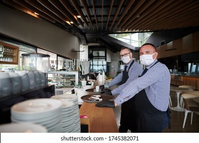 Waiter In A Medical Protective Mask Serves  The Coffee In Restaurant Durin Coronavirus Pandemic Representing New Normal Concept