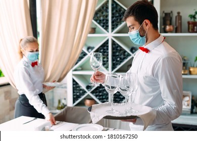 A Waiter In A Medical Protective Mask Serves A Table In The Restaurant. Employees Of A Restaurant Or Hotel In Protective Masks. The End Of Quarantine
