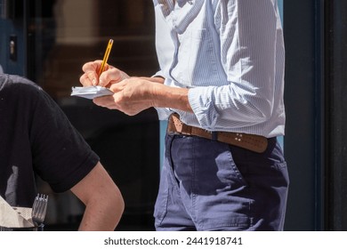 Waiter with no face visible writing down the order from guests in a restaurant at an outdoor terrace  - Powered by Shutterstock