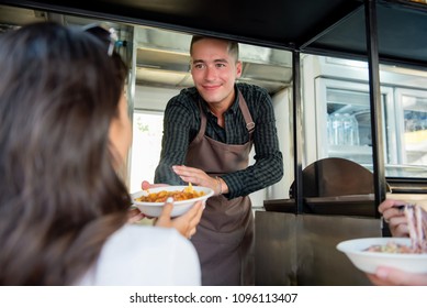 Waiter on food truck giving pasta in takeaway plate to woman customer - Powered by Shutterstock