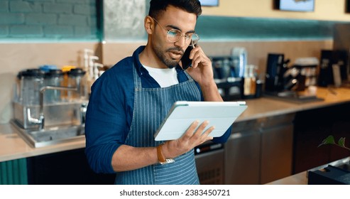 Waiter, phone call and tablet for restaurant communication, online management or customer service in cafe. Small business owner, barista or cashier man on mobile and digital tech for coffee shop data - Powered by Shutterstock