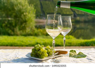 Waiter pouring  German quality white wine riesling, produced in Mosel wine regio from white grapes growing on slopes of hills in Mosel river valley in Germany, bottle and glasses served outside