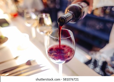 a waiter pouring glass of red wine on the table with some blurred stuff - Shutterstock ID 581076721
