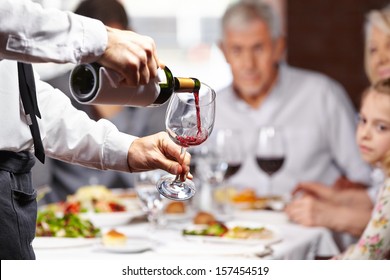 Waiter Pouring Red Wine In A Glass At A Restaurant Table