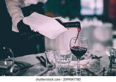 waiter pouring red wine into a glass in cafe or restaurant