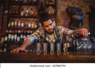 Waiter pouring tequila into shot glasses at counter in bar - Powered by Shutterstock