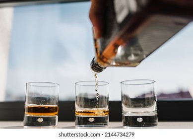 The Waiter Pours Alcohol Into Glasses. Many Glasses Of Whiskey, Scotch, Whisky, Brandy Served On Bar Table. Vintage Glass Of Filled With Bourbon, Cognac.