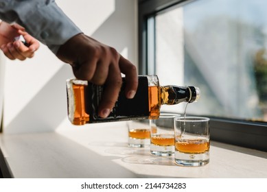 The Waiter Pours Alcohol Into Glasses. Many Glasses Of Whiskey, Scotch, Whisky, Brandy Served On Bar Table. Vintage Glass Of Filled With Bourbon, Cognac.