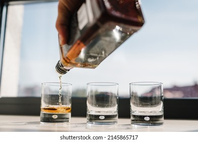 The Waiter Pours Alcohol Into Glasses. Many Glasses Of Whiskey, Scotch, Whisky, Brandy Served On Bar Table. Vintage Glass Of Filled With Bourbon, Cognac.