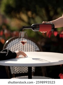 Waiter pours ruby wine into bordeaux glass. Burgundy wineglass with red wine in female hand on table. Wine tasting. Aperitif. Alcohol beverage. Drink concept. Autumn atmosphere. Dinner in restaurant.