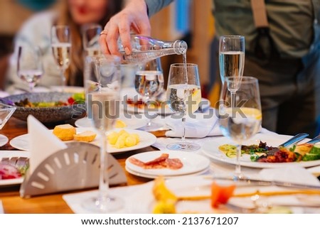 a waiter pours water into a glass. mineral water instead of wine. the tradition of toasting and drinking alcohol on holidays.