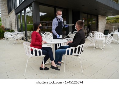 Waiter With Protective Medical Mask And Gloves Serving Guest With Coffee At An Outdoor Bar Café Or Restaurant New Normal Concept Reopening After Quarantine