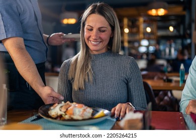 The Waiter In The Restaurant Brings Lunch To The Whole Family Of Three. Family Launch Concept.