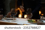 The waiter serves the couple their main course and wine while they wait for their order in the luxury restaurant. Candles lit near the dining table provide a dim and pleasant atmosphere.
