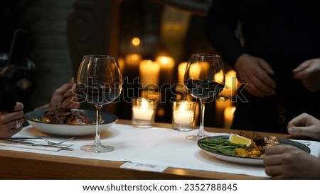 The waiter serves the couple their main course and wine while they wait for their order in the luxury restaurant. Candles lit near the dining table provide a dim and pleasant atmosphere.