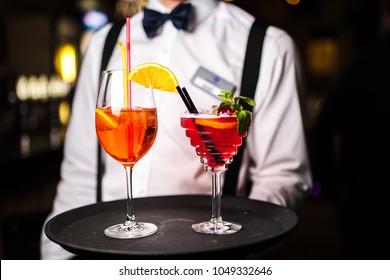The waiter serves two cocktails on a tray. Close-up orange and red cocktails with orange and mint. - Powered by Shutterstock