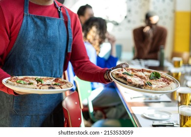 Waiter serving delicious pizza in cozy pizzeria restaurant - Italian pizza in italian restaurant - Hands of waiter holding two pizzas Margherita - Original recipe of italian tasty pizza margherita