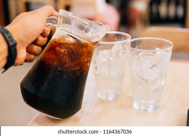 Waiter Serving Drinks. Handle Pour Cola Jug To Two Ice Glass On Table.