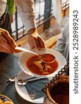 Waiter is serving a fish soup in a plate for a guest. Old fish restaurant.