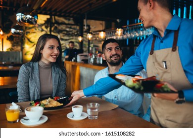 Waiter Serving Food To A Customers In Restaurant