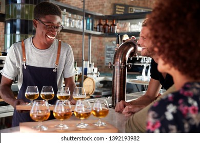 Waiter Serving Group Of Friends Beer Tasting In Bar