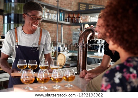 Waiter Serving Group Of Friends Beer Tasting In Bar