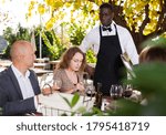 Waiter serving meals to friendly company at open-air restaurant