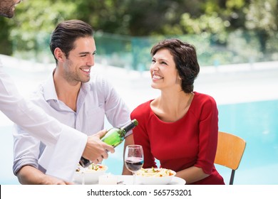 Waiter Serving Red Wine To Couple At Poolside