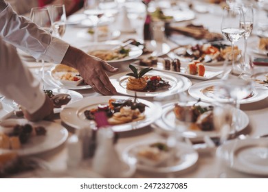 Waiter serving table in the restaurant preparing to receive guests. Waiter carrying plates with meat dish on some festive event.  - Powered by Shutterstock