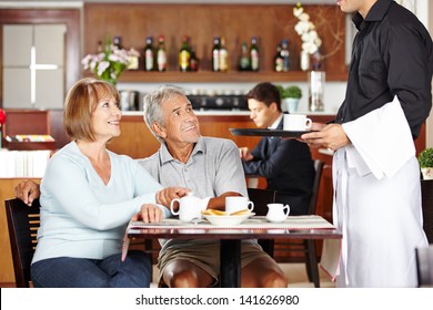 Waiter Serving Two Seniors In A Coffee Shop For Breakfast