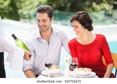 Waiter Showing Wine Bottle To Couple At Poolside