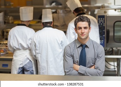 Waiter Standing In A Busy Kitchen With Three Chefs Behind Him