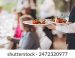 waiter in a stylish uniform carrying an exquisite dish to a client in a beautiful gourmet restaurant. Table service in the restaurant.