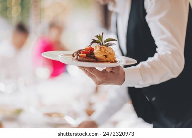 waiter in a stylish uniform carrying an exquisite dish to a client in a beautiful gourmet restaurant. Table service in the restaurant. - Powered by Shutterstock