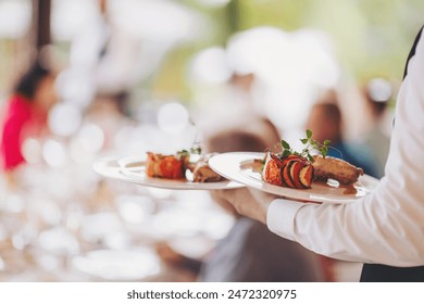 waiter in a stylish uniform carrying an exquisite dish to a client in a beautiful gourmet restaurant. Table service in the restaurant. - Powered by Shutterstock