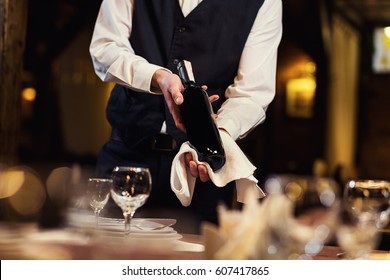 The waiter in uniform with a white towel offers visitors wine in restaurant - Powered by Shutterstock