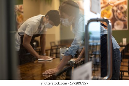 Waiter wearing protective face mask while cleaning tables in restaurant - Powered by Shutterstock