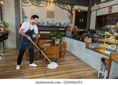 Waiters handsome Indian wearing apron mopping the floor in cafe and bakery preparing to support customers come in restaurant. Cleaning store before closing coffee shop. Small business owner concept. - Powered by Shutterstock