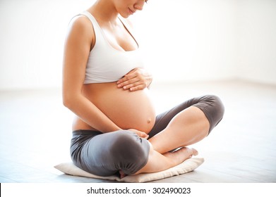 Waiting for a baby. Close-up of pregnant woman touching her belly while sitting in lotus position