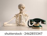 Waiting concept. Human skeleton at table with corded telephone against light grey background