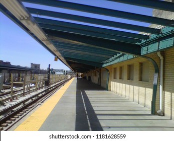 Waiting For The NYC Subway Platform For A Train To Come On A Beautiful Sunny Day. Above Ground Tracks, Open Air Roof Creating Shadows. Blue, Green, And Yellow.