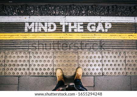 Waiting for the subway train at the station from the platform seeing the Mind the Gap letters